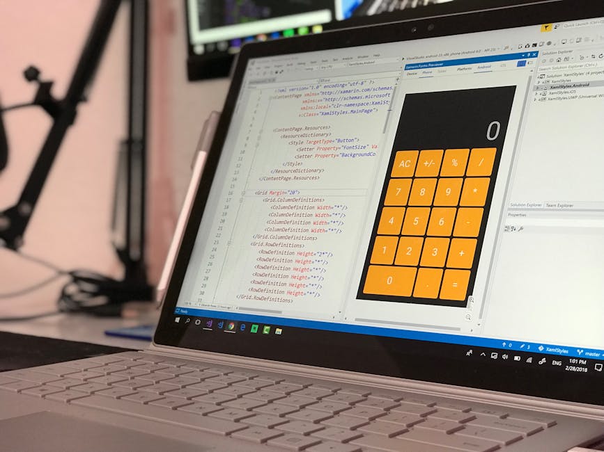A close-up of a laptop computer with an open screen displaying lines of code in various colors, alongside a large digital calculator with an orange keypad and black display. The keyboard is white with